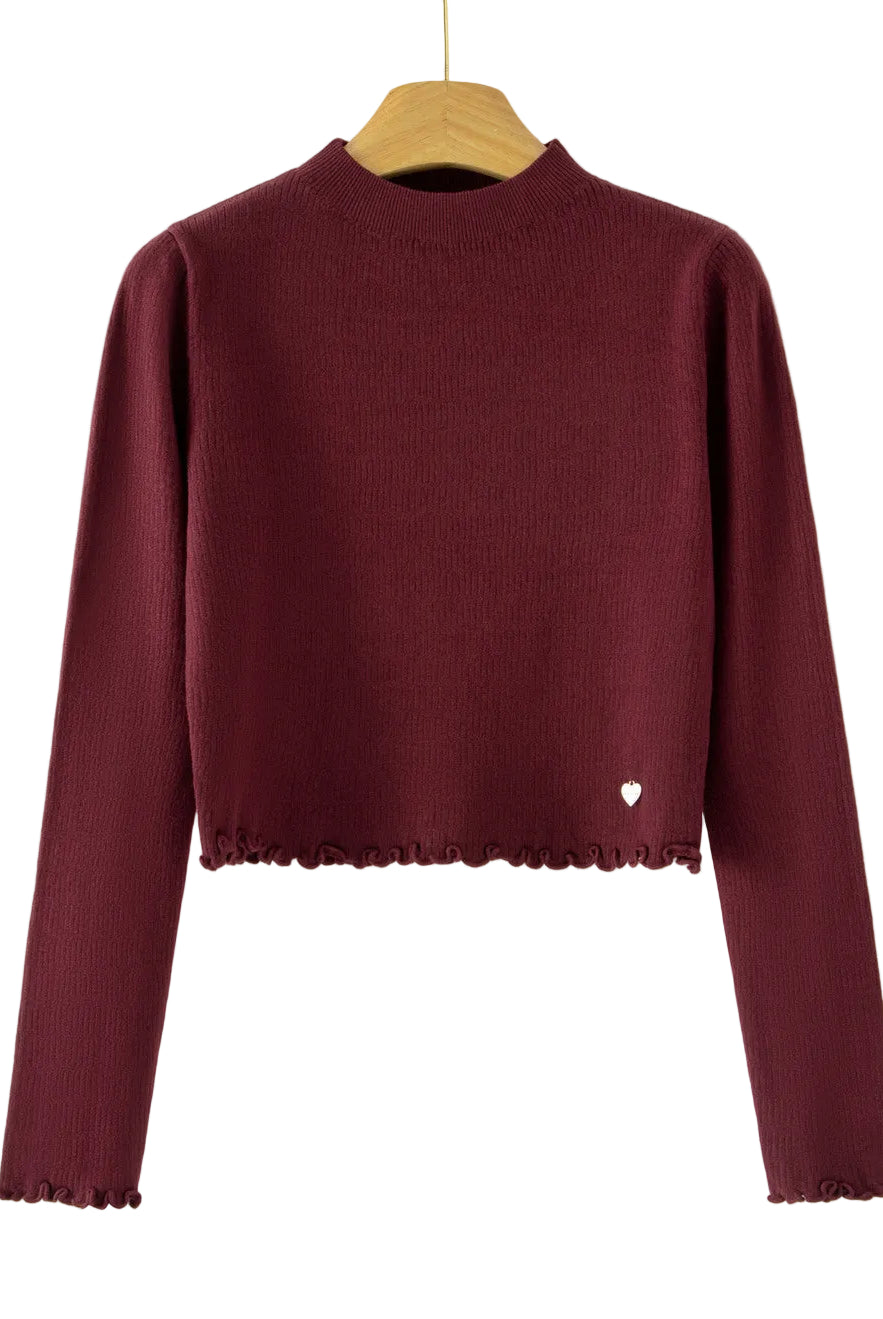 A long-sleeve ribbed knit mock-neck sweater in deep burgundy, hanging on a wooden hanger against a plain white background. The bottom hem has a scalloped edge, and a small white heart detail is visible on the lower right side.