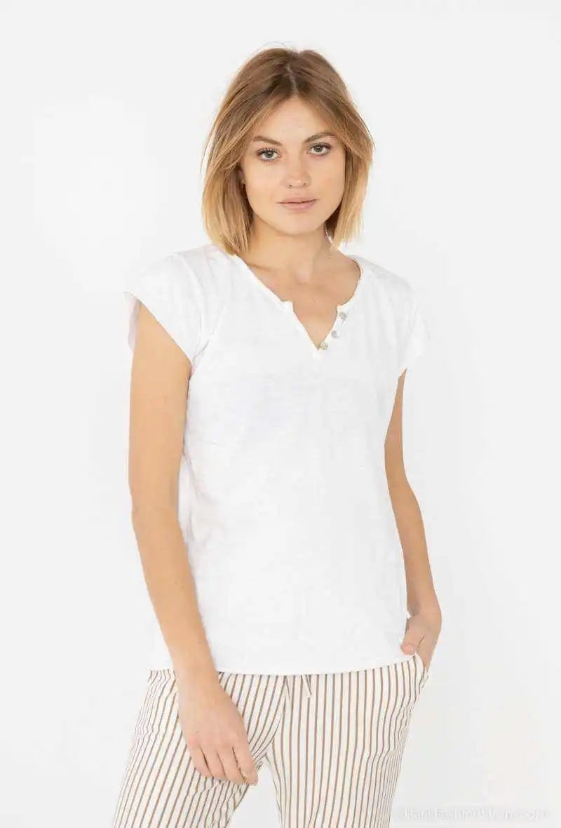 A woman modeling a white short-sleeve henley top with a split V-neck and drawstring detail, paired with beige and white vertically striped pants, against a plain white studio background.