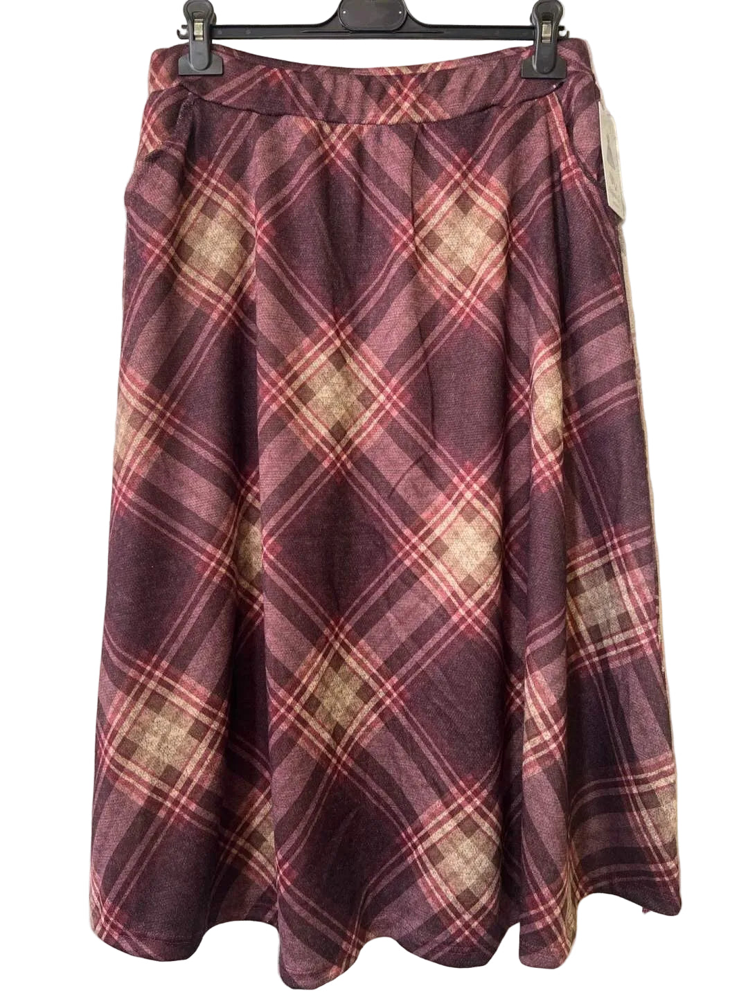 A pleated A-line skirt in a burgundy and beige plaid pattern, hanging on a black hanger against a textured gray wall.