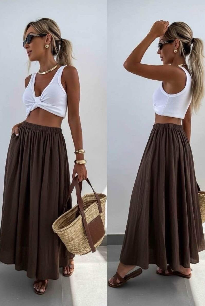 Woman wearing a white top and brown skirt with a straw bag indoors.