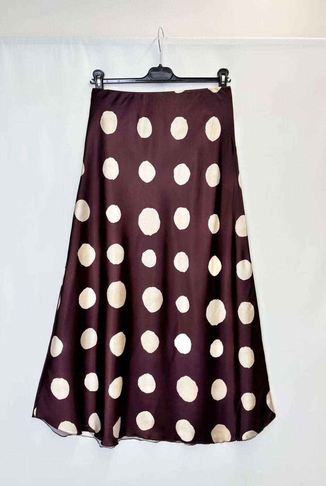 A dark plum purple satin skirt with large cream polka dots, hanging on a black hanger against a white fabric backdrop.