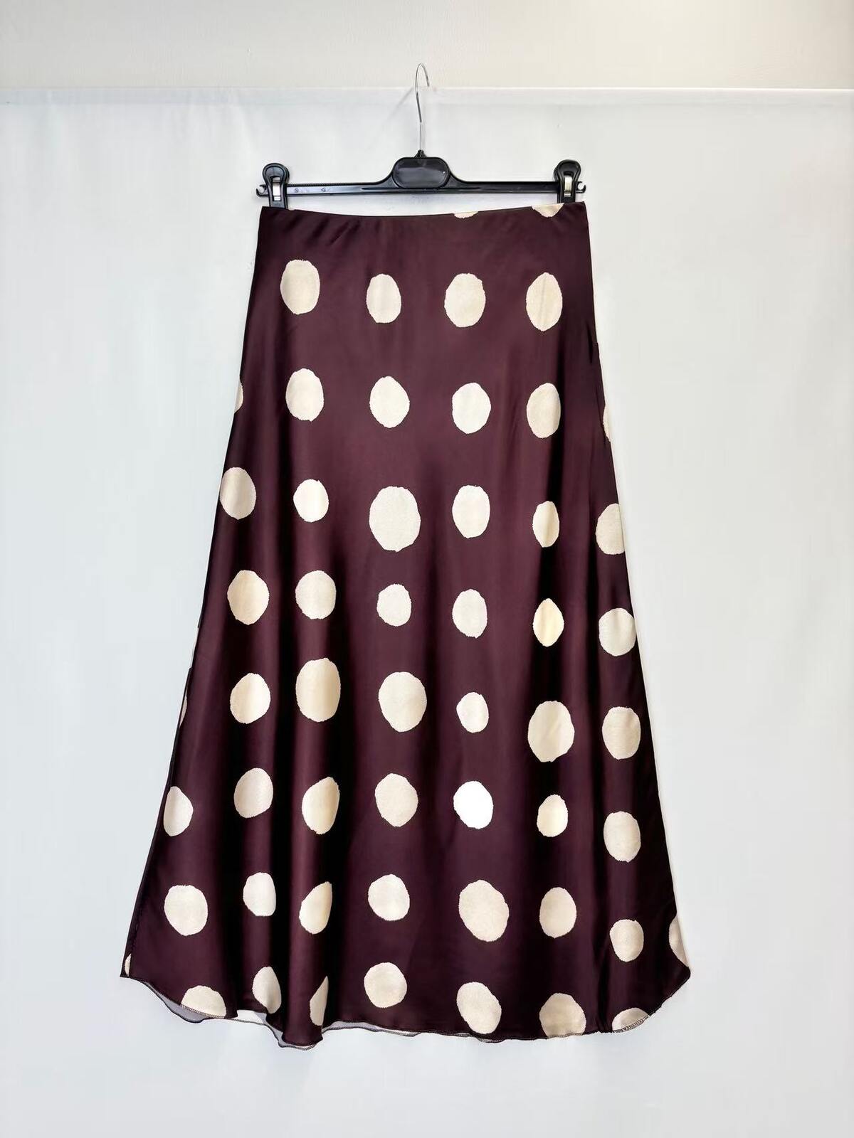 A dark plum purple satin skirt with large cream polka dots, hanging on a black hanger against a white fabric backdrop.