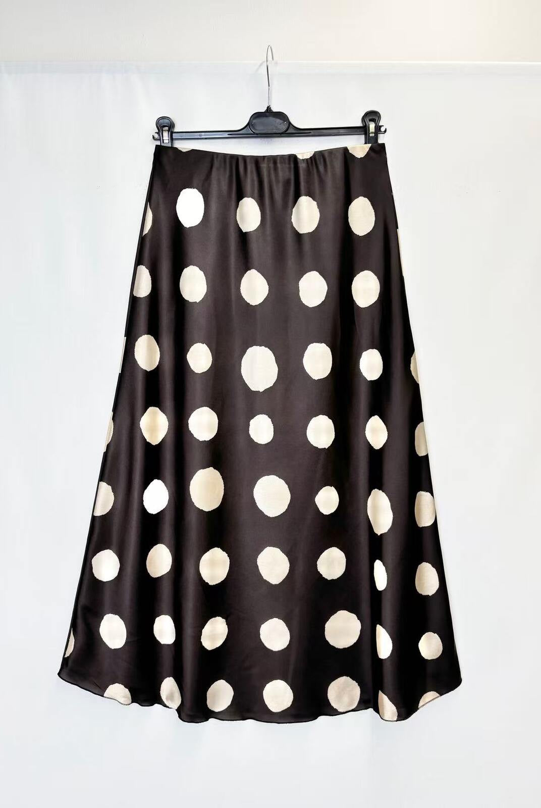 A black satin midi skirt with large cream polka dots, hanging on a black hanger against a white background.