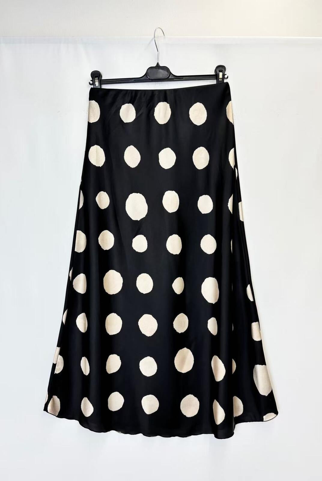 A black A-line skirt with large beige polka dots, hanging on a black hanger against a white studio backdrop.