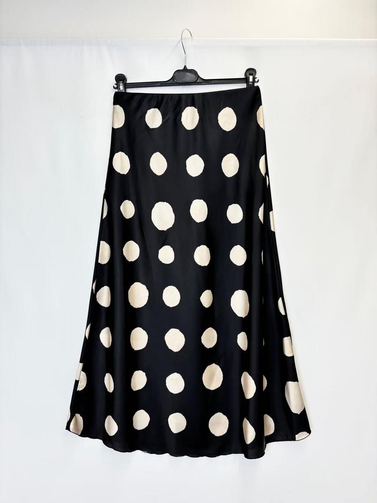 A black A-line skirt with large beige polka dots, hanging on a black hanger against a white studio backdrop.