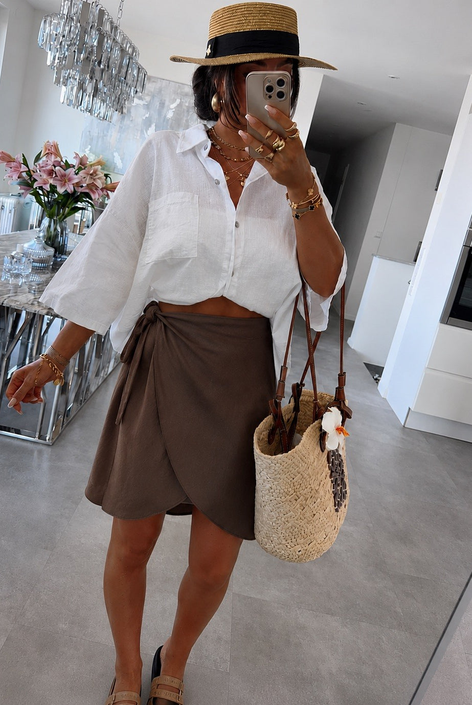 A woman wearing a white cropped button-up shirt, a brown wrap-style mini skirt