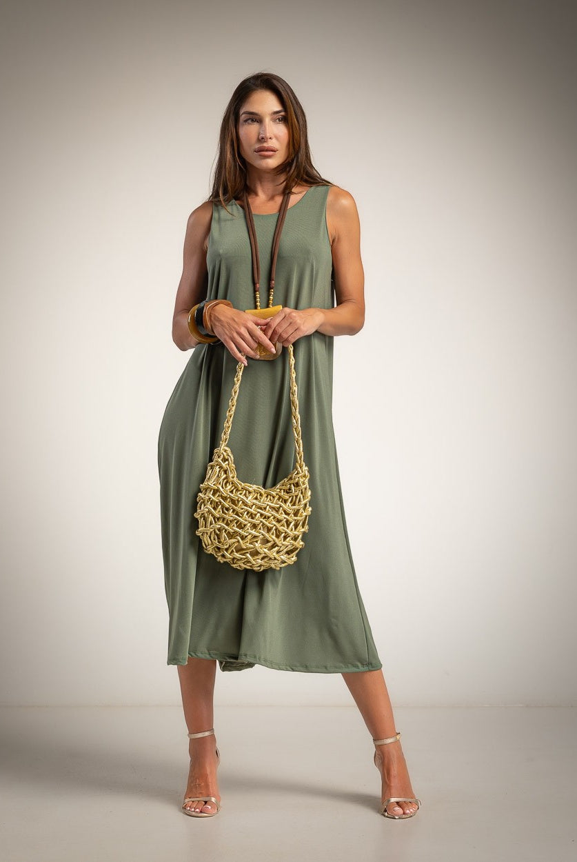 A woman modeling a sleeveless olive green midi dress, holding a chunky woven tan shoulder bag