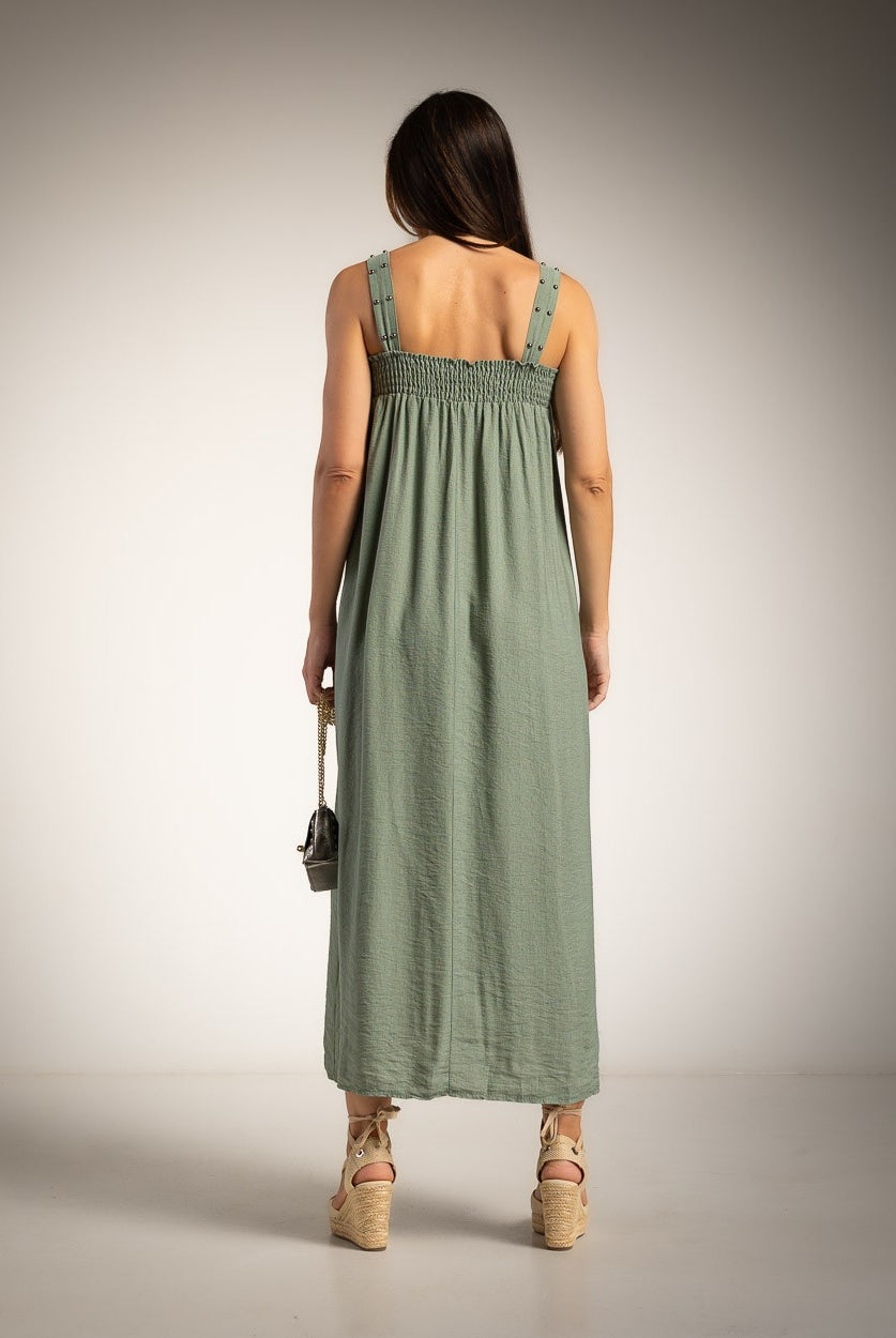 A woman viewed from behind wearing a green sleeveless maxi dress with a smocked bodice and straps