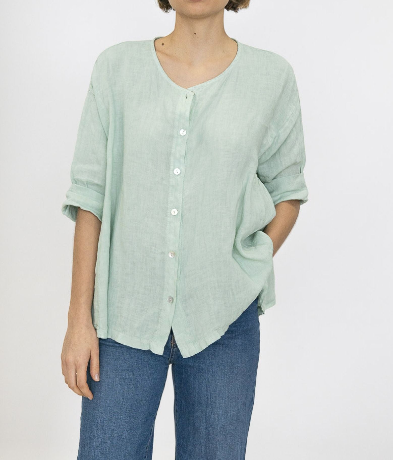 Person wearing a light green button-up shirt and blue jeans on a white background