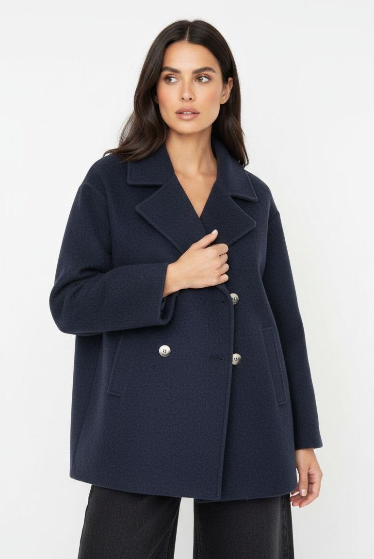 A woman modeling a navy blue double-breasted coat with silver buttons, photographed against a clean white studio background.