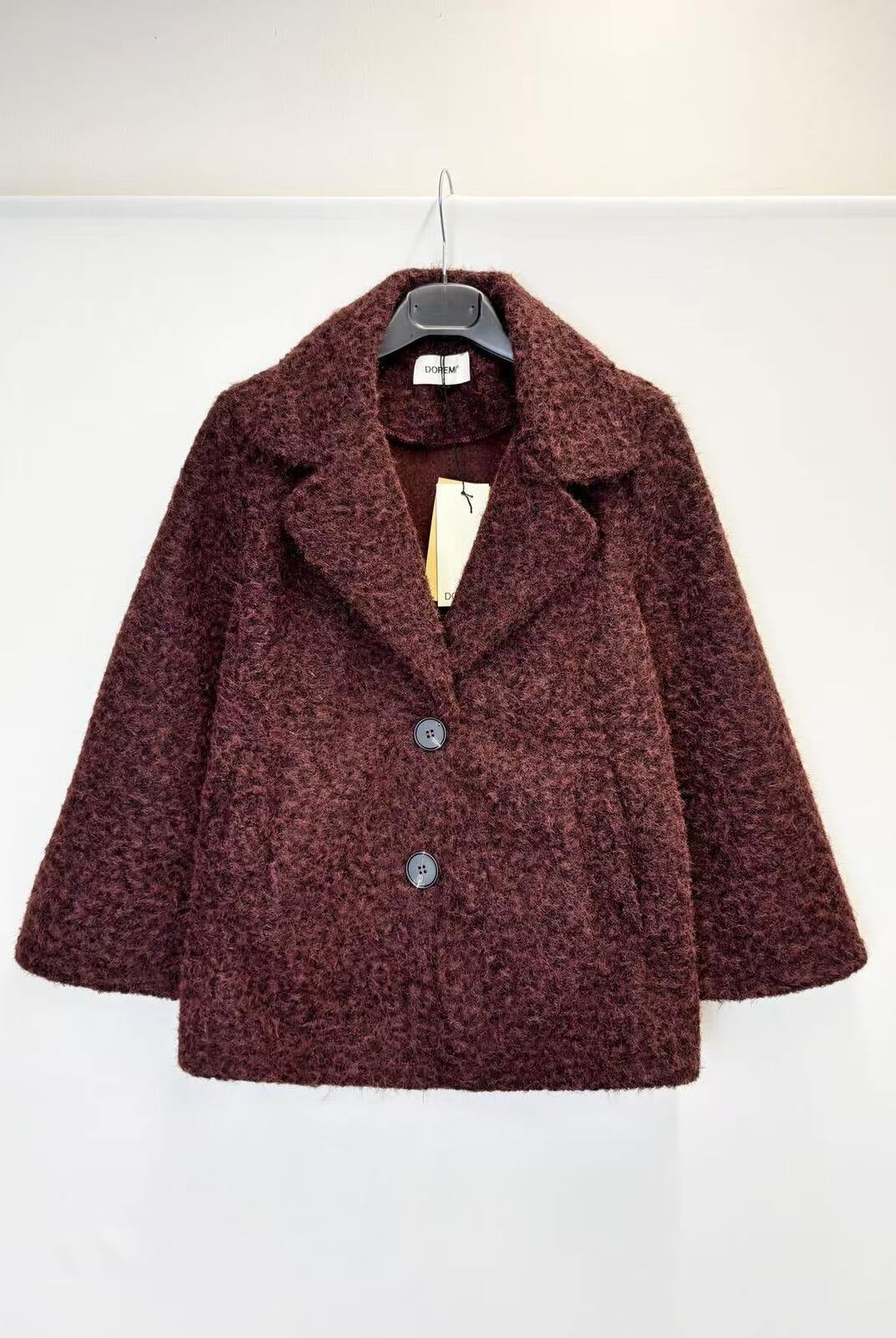 A textured, boucle-style dark burgundy coat with wide lapels and two front buttons, hanging on a black hanger against a plain white wall.
