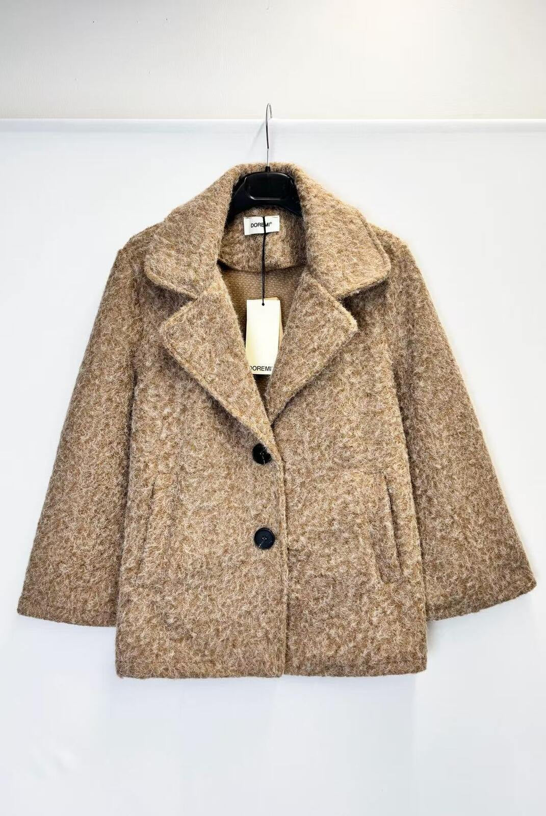 A textured beige tweed coat with a double-breasted design, hanging on a black hanger against a plain white wall.