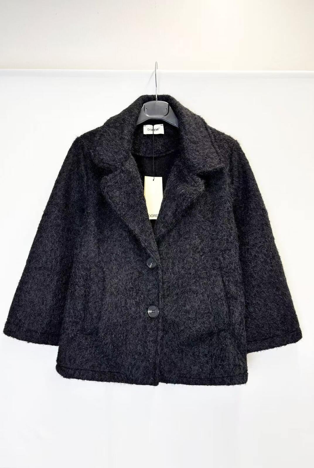 A dark charcoal gray textured wool-blend jacket with a wide collar and three front buttons, hanging on a black hanger against a plain white wall.