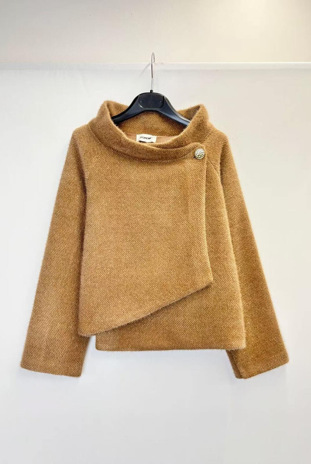 A camel brown fuzzy asymmetrical wrap sweater hanging on a black hanger against a plain white wall.