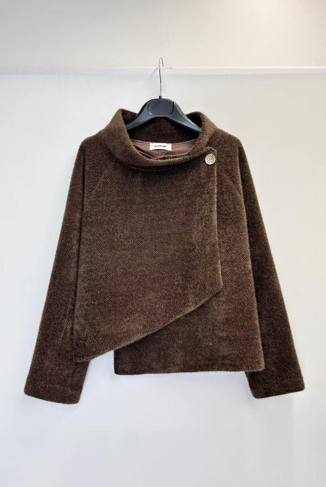 A brown textured wrap jacket with a high mock neck and asymmetrical button detail, hanging on a black hanger against a plain white wall.