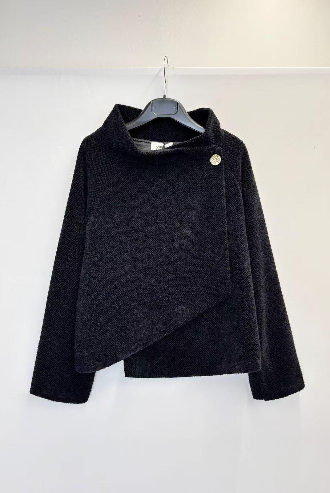 A black textured wrap-style jacket with a high mock neck and asymmetrical button closure, hanging on a black hanger against a plain white wall.