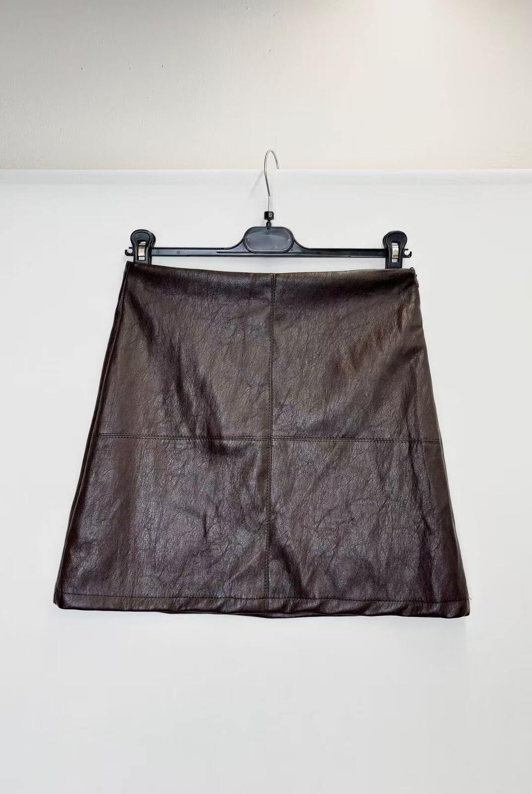 A dark brown faux-leather A-line mini skirt with a crinkled texture, hanging on a black hanger against a plain white wall.