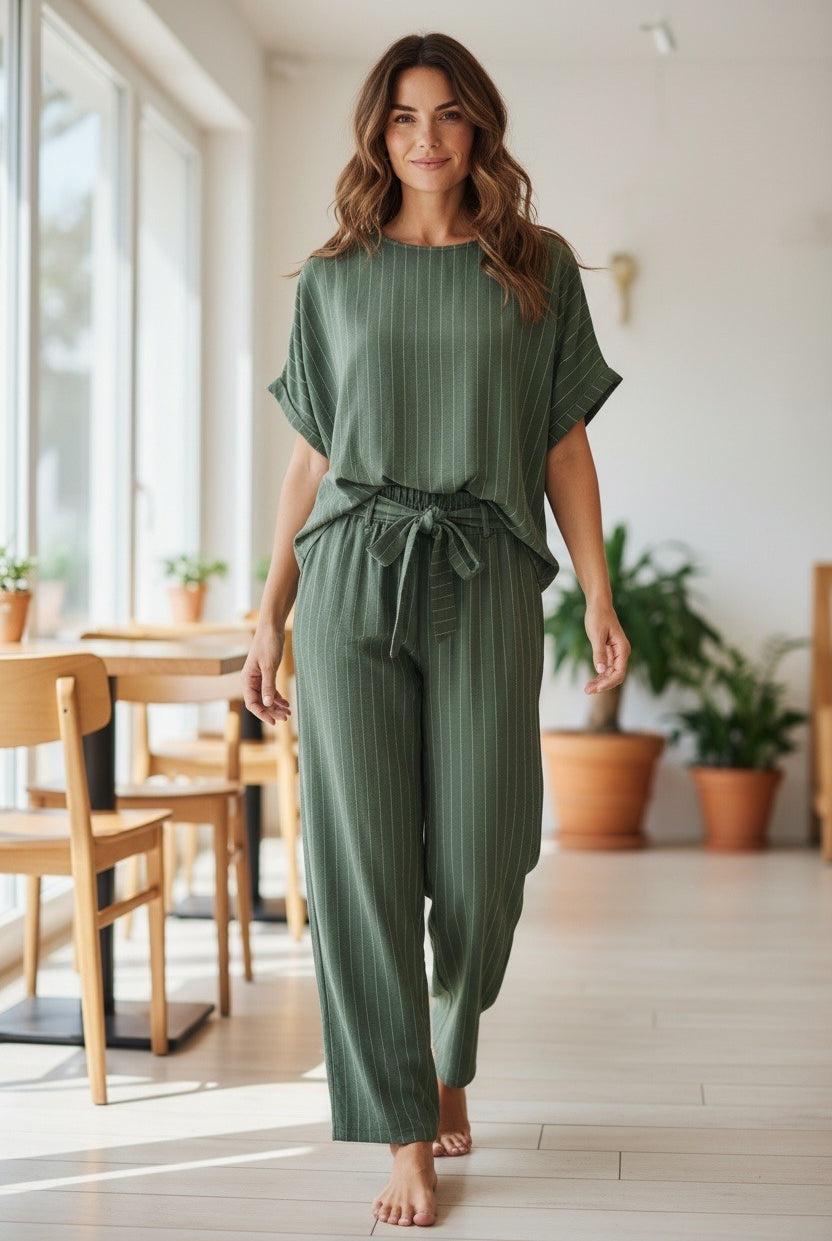 Woman wearing a green jumpsuit in a bright room with large windows and plants.