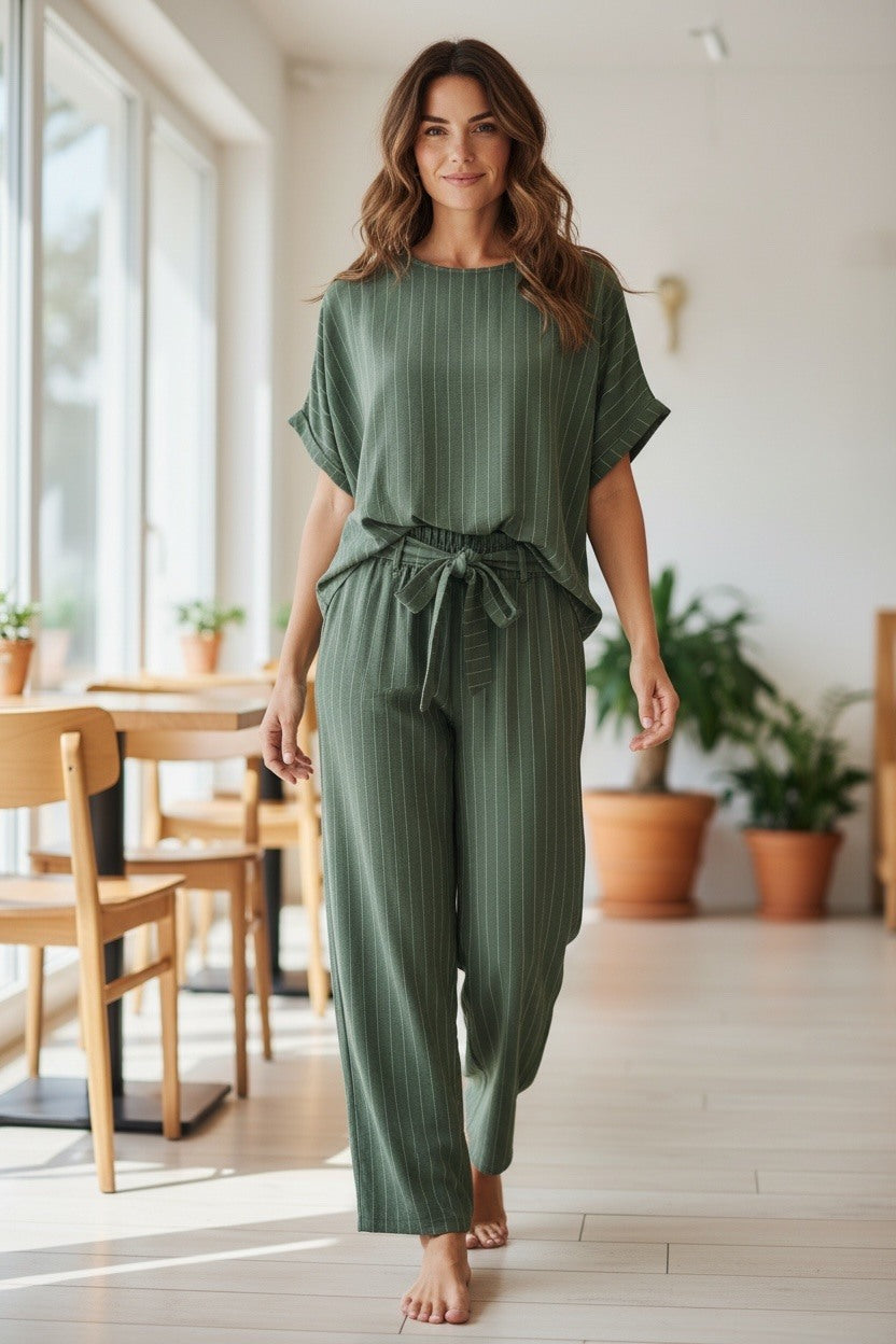 Woman wearing a green jumpsuit in a bright room with large windows and plants.