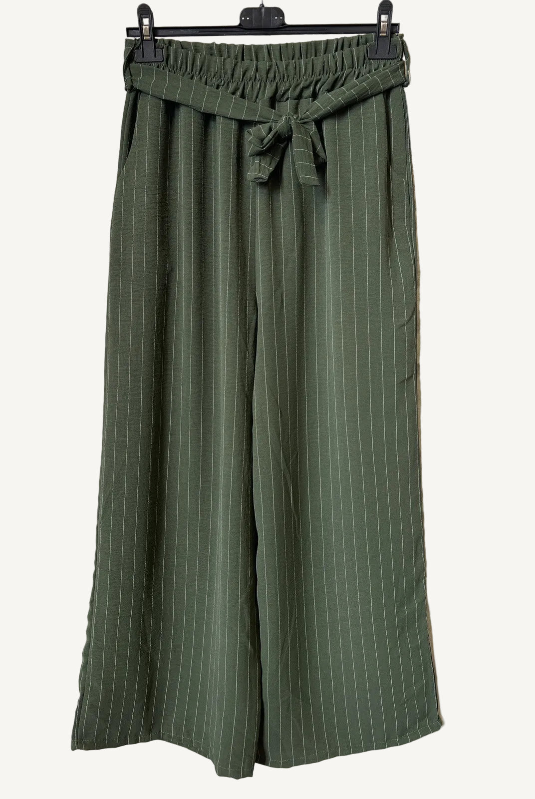 Green striped pants hanging on a rack against a textured white background
