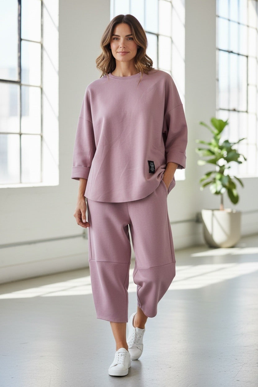 Woman wearing a pink outfit standing in a bright room with large windows.