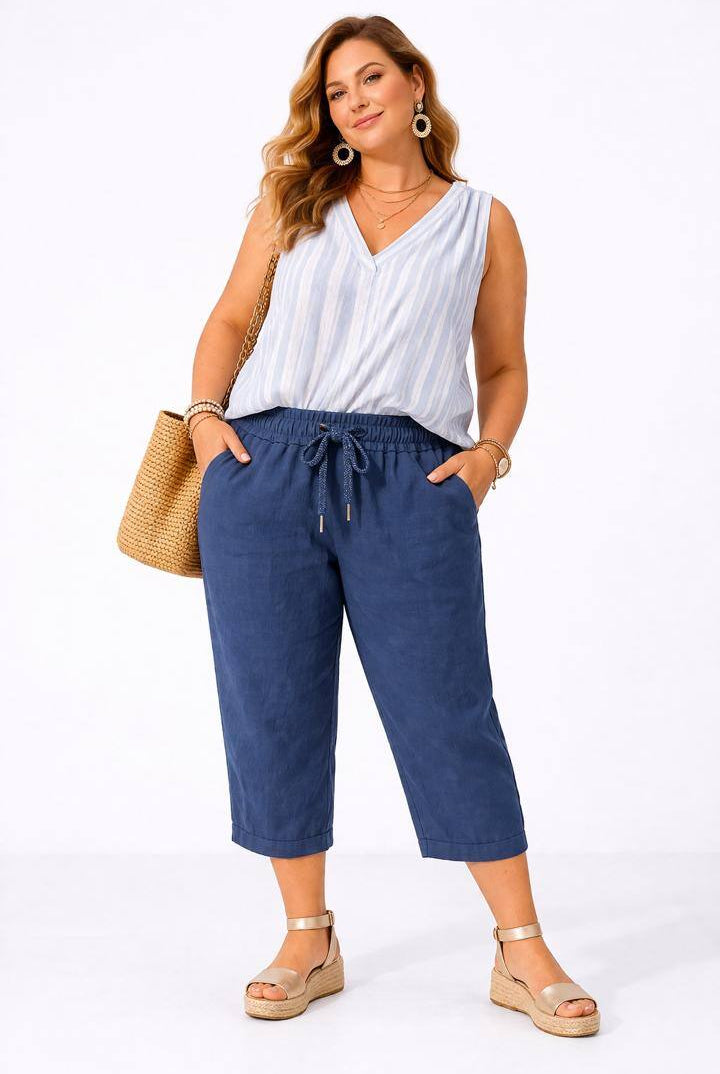 Woman wearing a white sleeveless top and navy blue pants, standing against a white background.