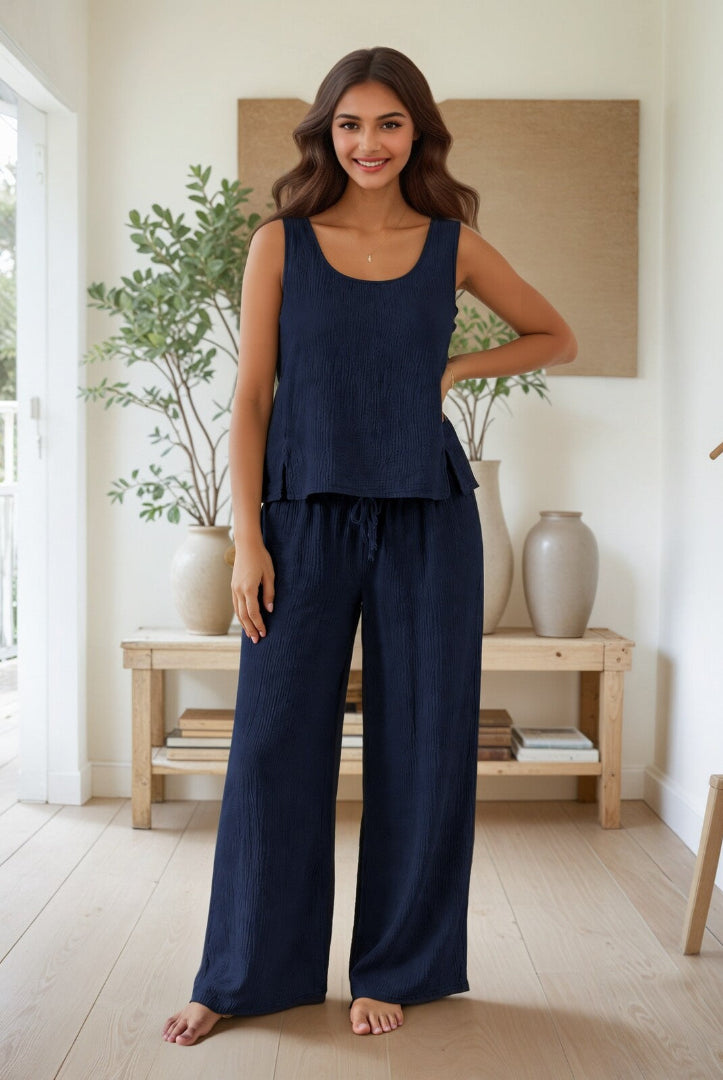 Woman wearing a navy blue outfit standing in a bright room with plants and a wooden shelf.