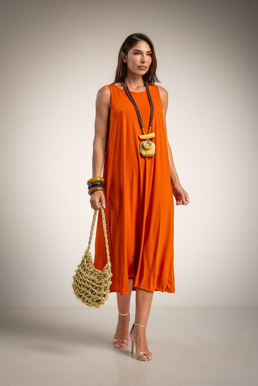 A woman models a sleeveless bright orange midi dress, holding a small woven straw bag.