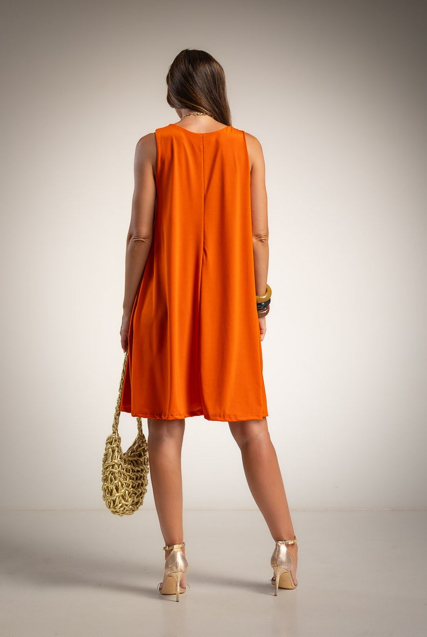 A woman shown from behind wearing a sleeveless bright orange A-line dress, holding a woven gold handbag