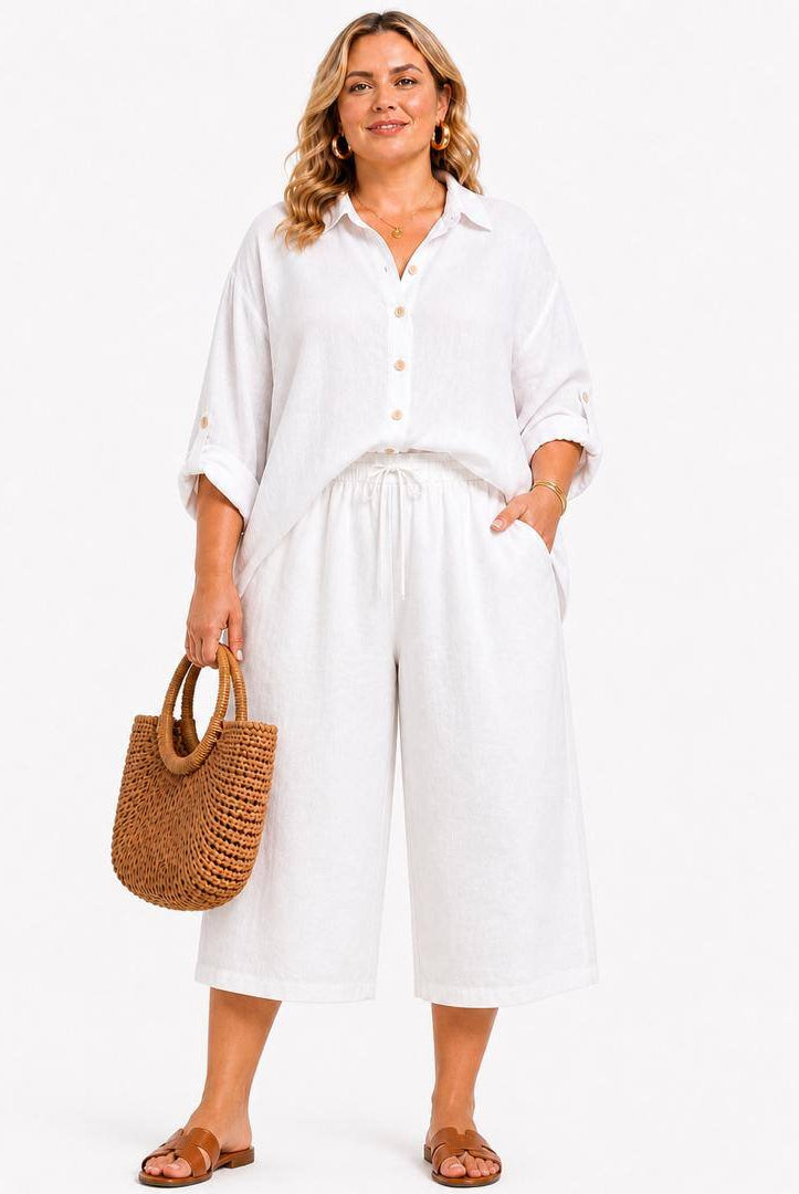 Woman wearing a white outfit with wide-leg pants and a straw bag on a white background