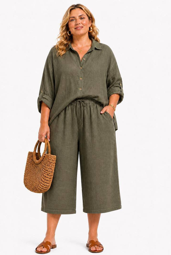 Woman wearing a green pair of loose fitting cropped trousers holding a woven bag on a white background