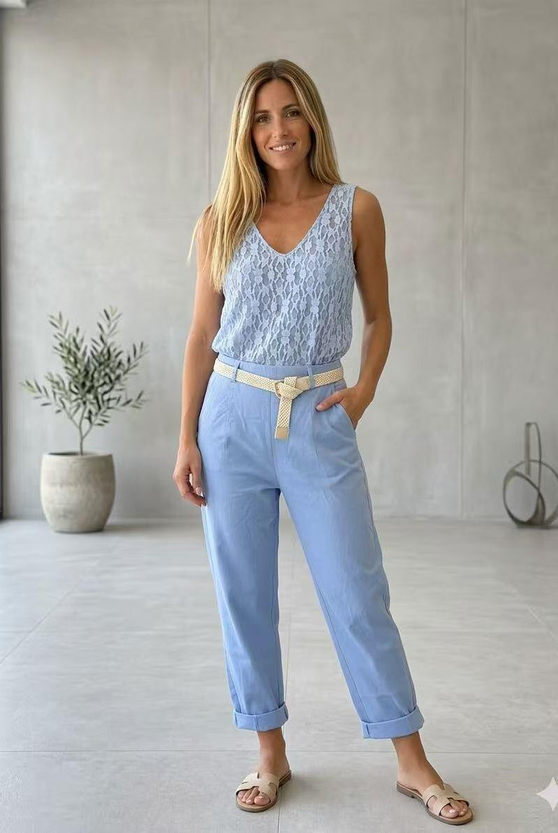 Woman wearing a light blue sleeveless top and pants in a minimalistic room.