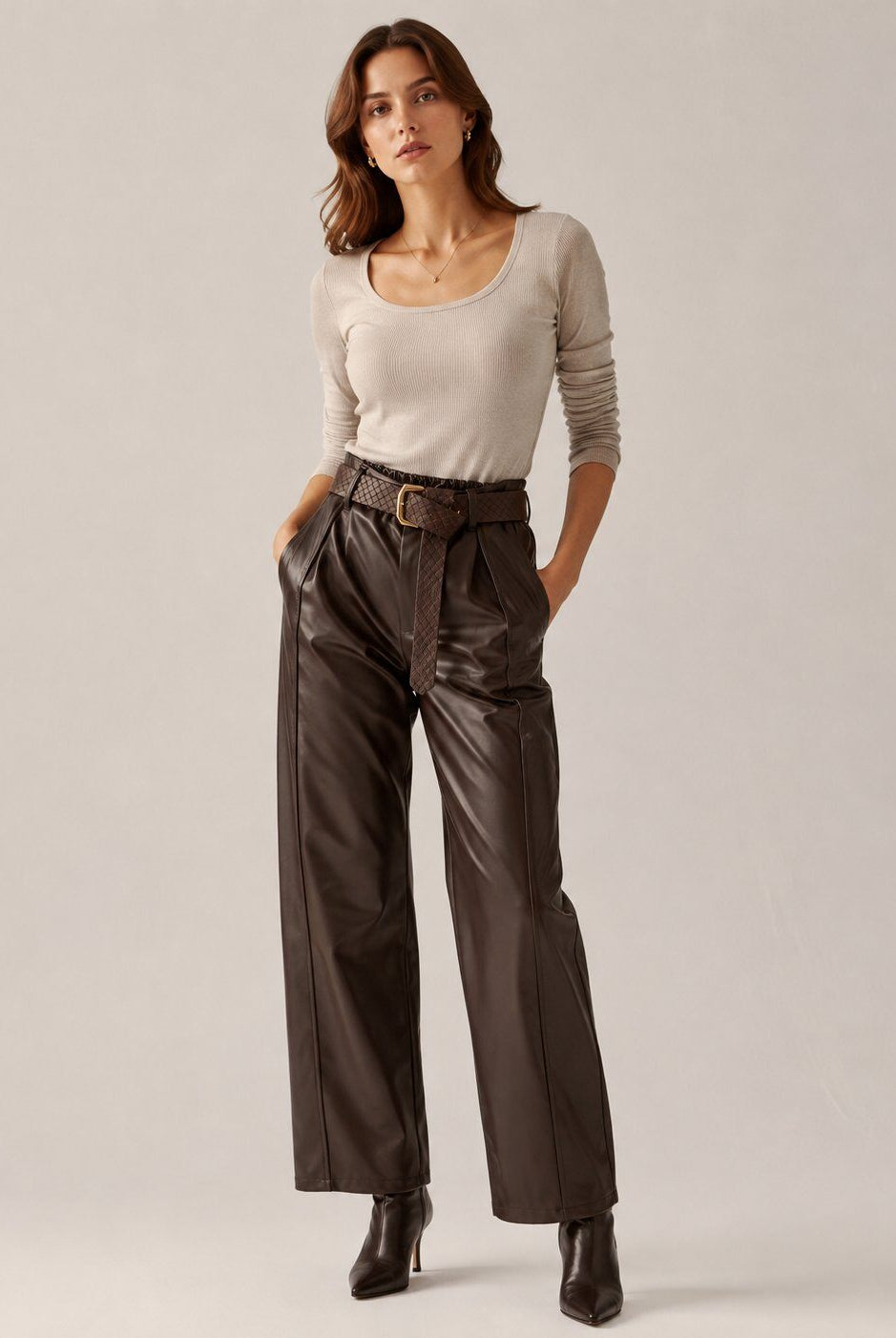 A woman modeling a beige long-sleeve scoop-neck top and dark brown wide-leg faux-leather trousers with a matching belt, paired with black ankle boots