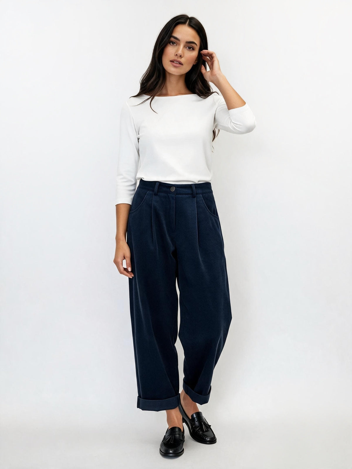A woman modeling a white long-sleeve top and navy wide-leg cropped trousers with black loafers, standing against a plain white studio background.