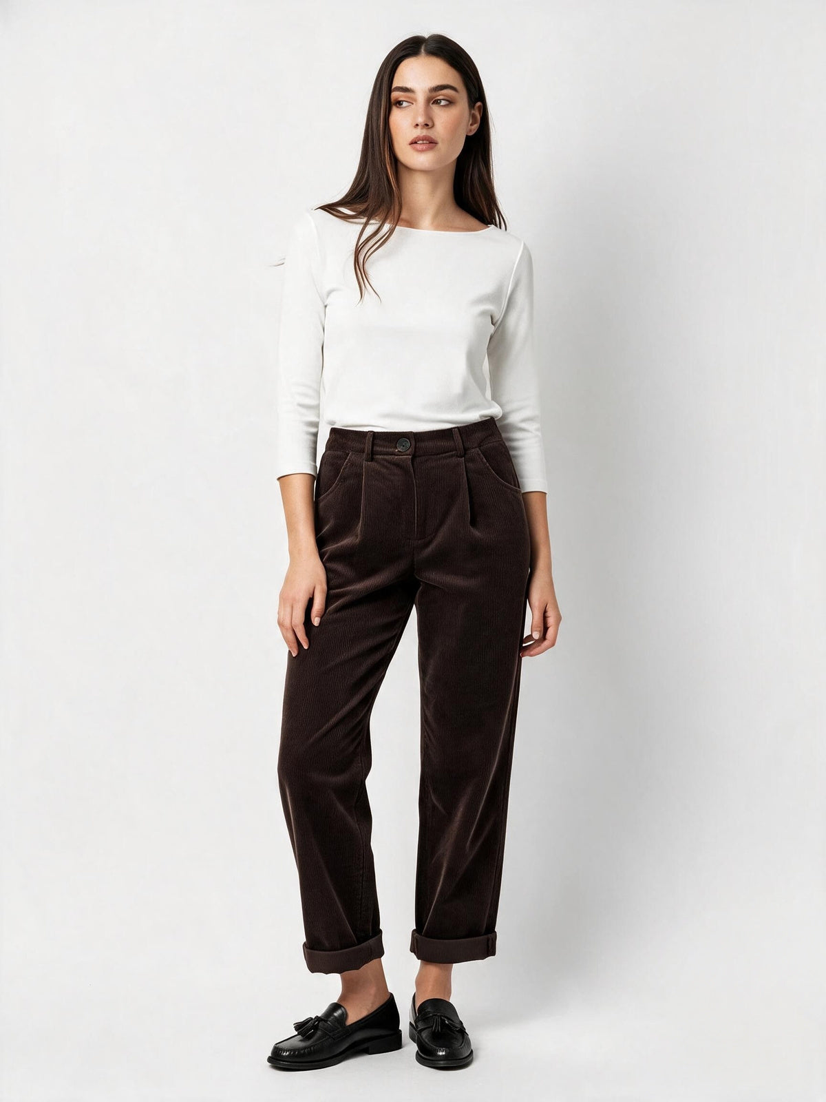A woman modeling a white long-sleeve top and dark brown corduroy trousers with black loafers