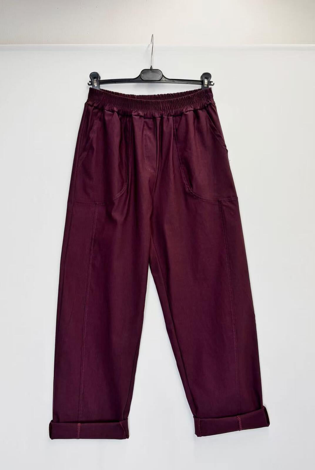 A pair of dark burgundy wide-leg pants with an elastic waistband, hanging from a black hanger against a plain white wall.