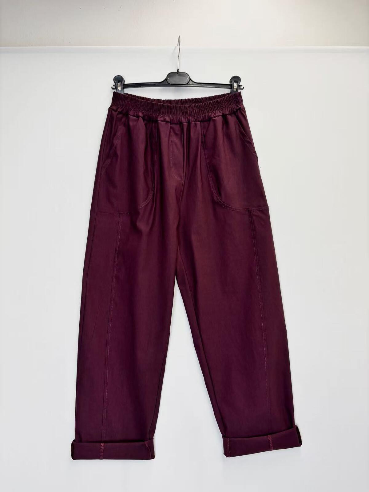 A pair of dark burgundy wide-leg pants with an elastic waistband, hanging from a black hanger against a plain white wall.