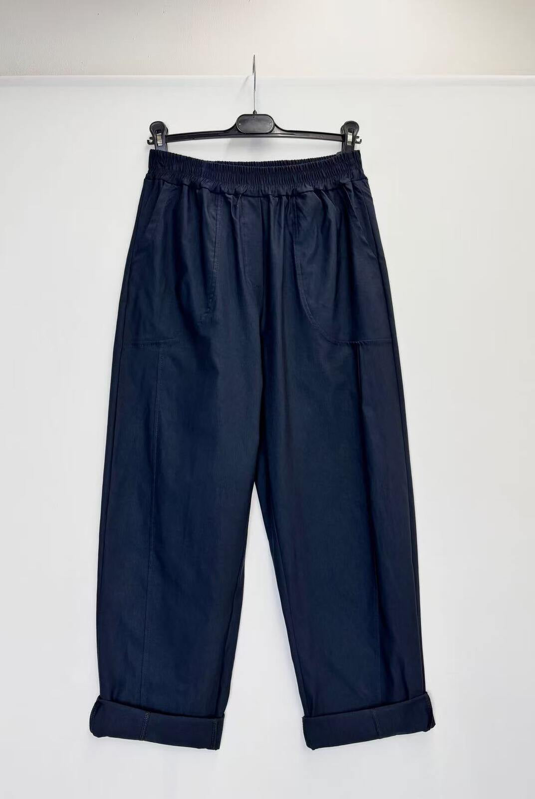 A pair of dark navy blue cropped pants with an elastic waistband and rolled cuffs, hanging on a black hanger against a plain white wall.