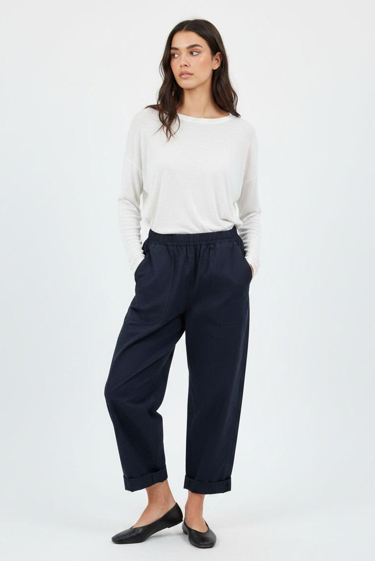 A woman modeling a pair of dark navy wide-leg cropped trousers with a drawstring waist, paired with a white long-sleeve top and black flats, against a plain white studio background.