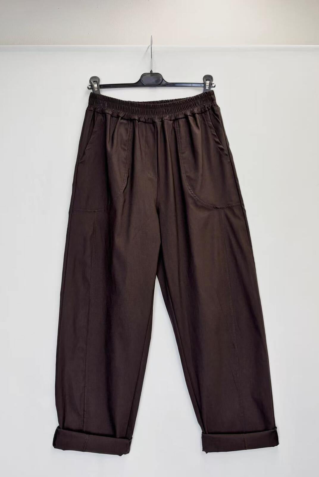 Dark brown wide-leg pants with an elastic waistband and cuffed hems, hanging on a black hanger against a plain white wall.