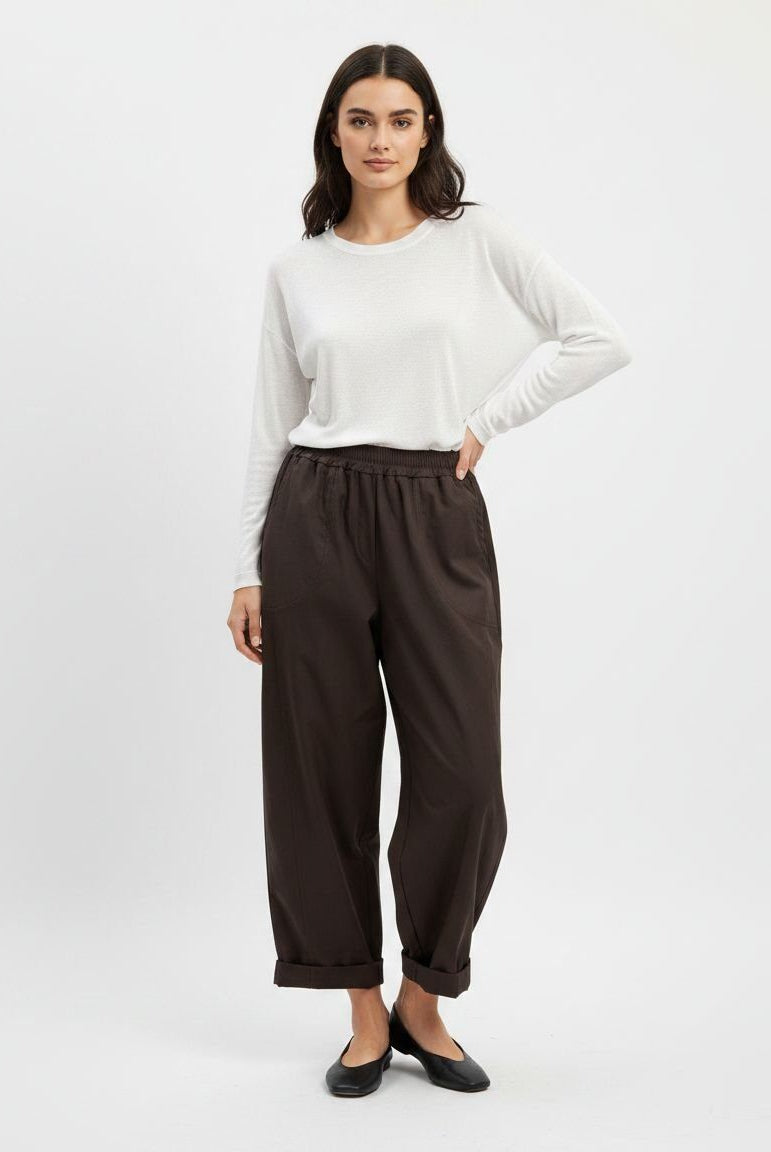 A woman modeling a white long-sleeve top and dark brown wide-leg cropped pants with black flats, standing against a light gray studio background.