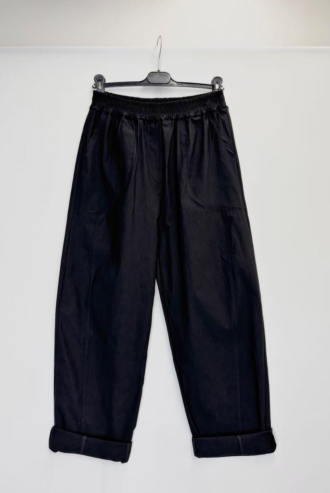 Black wide-leg cropped pants with an elastic waistband and rolled cuffs, hanging on a black hanger against a plain white wall.