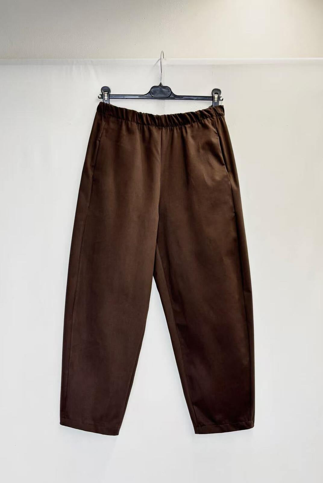 A pair of dark brown wide-leg trousers hanging from a black hanger against a plain white wall.