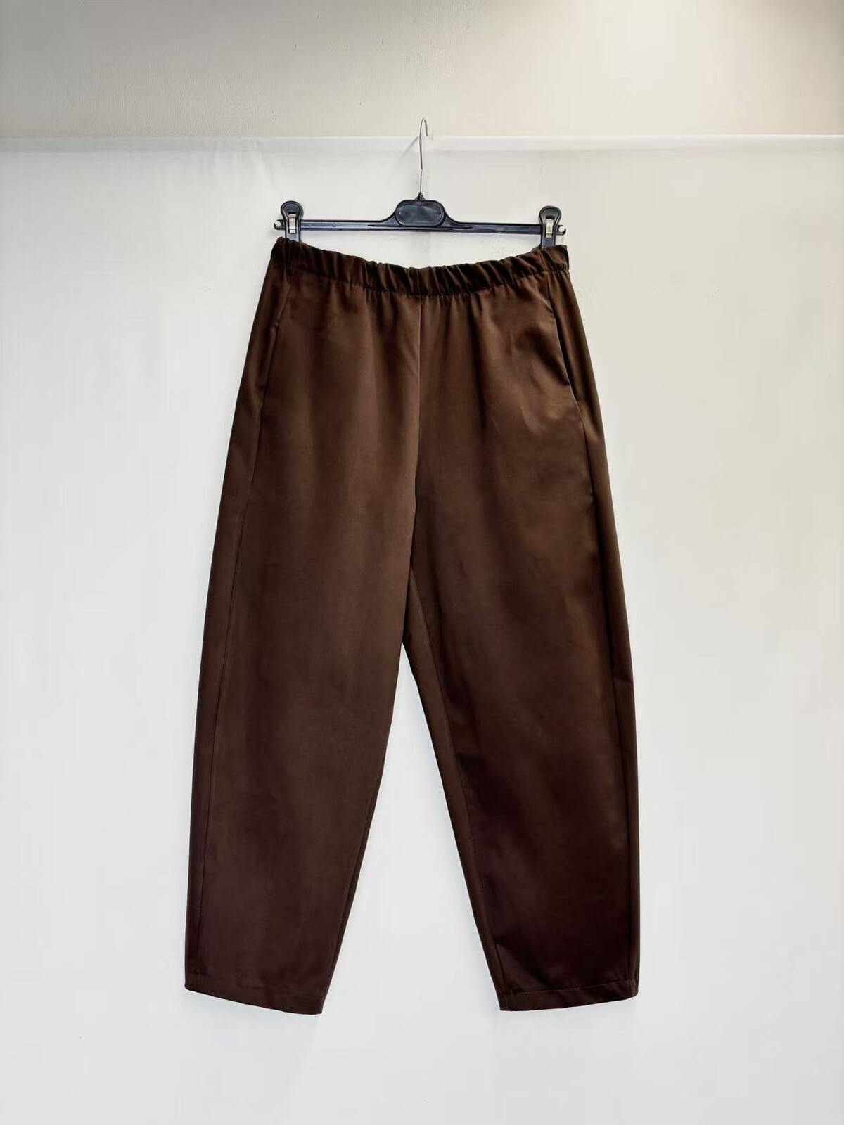 A pair of dark brown wide-leg trousers hanging from a black hanger against a plain white wall.