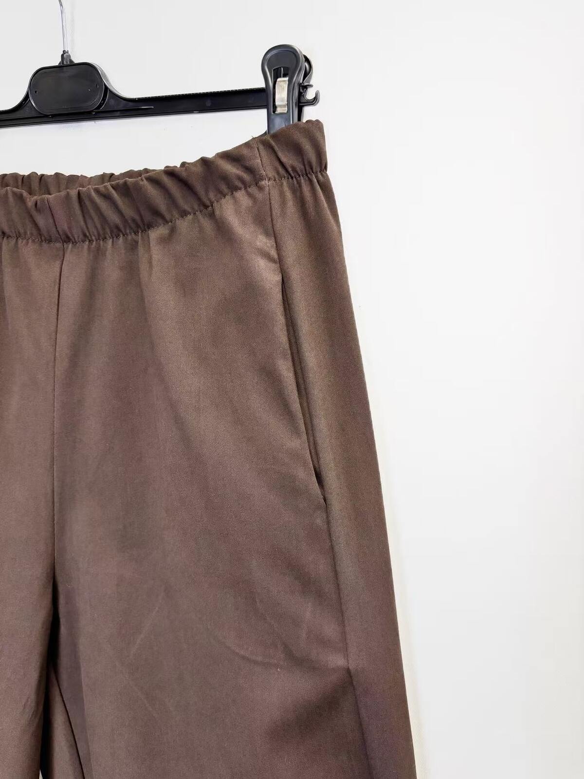 Brown wide-leg trousers with an elastic waistband, hanging on a black hanger against a plain white wall.