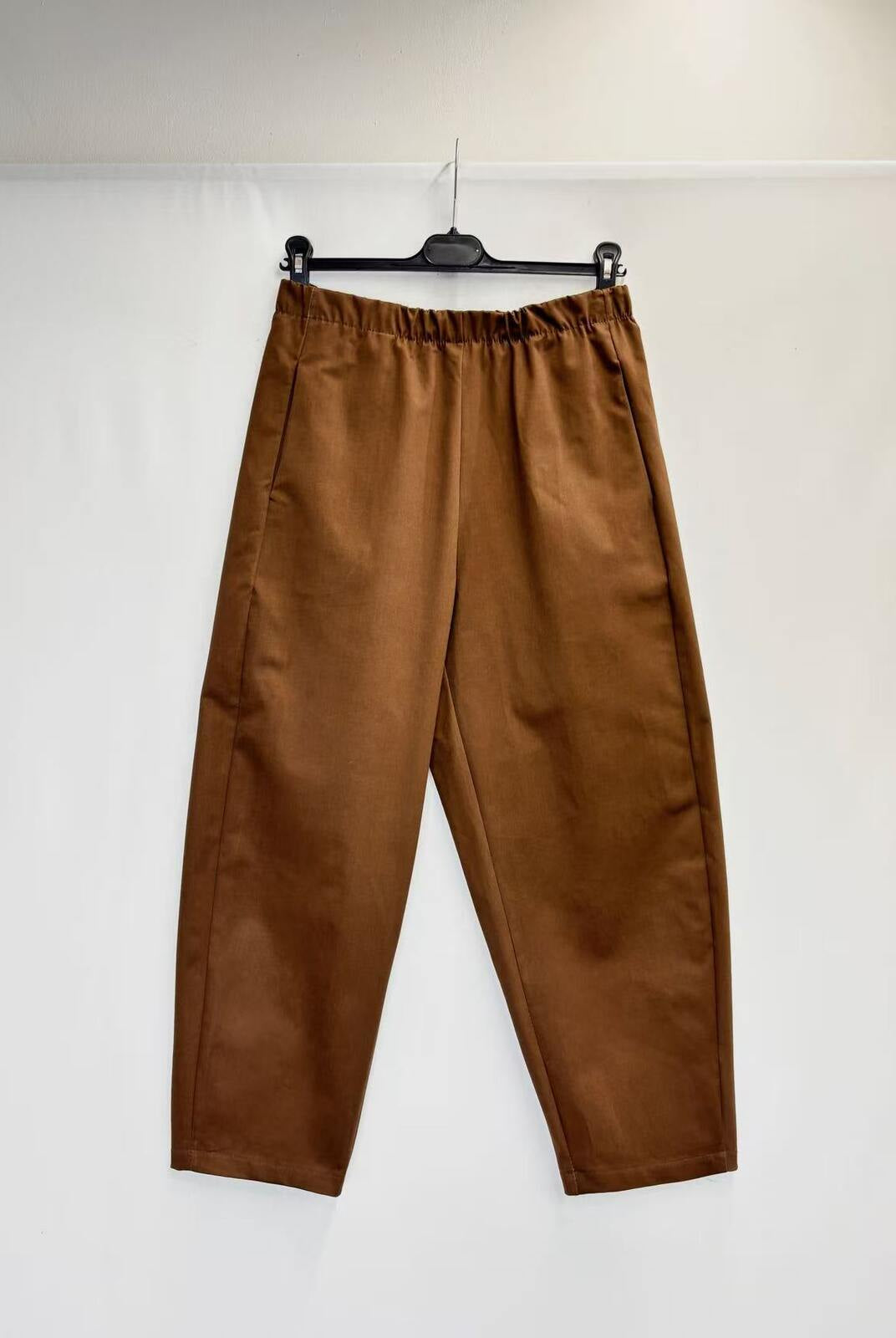 A pair of brown wide-leg cropped pants with an elastic waistband, hanging from a black hanger against a plain white backdrop.