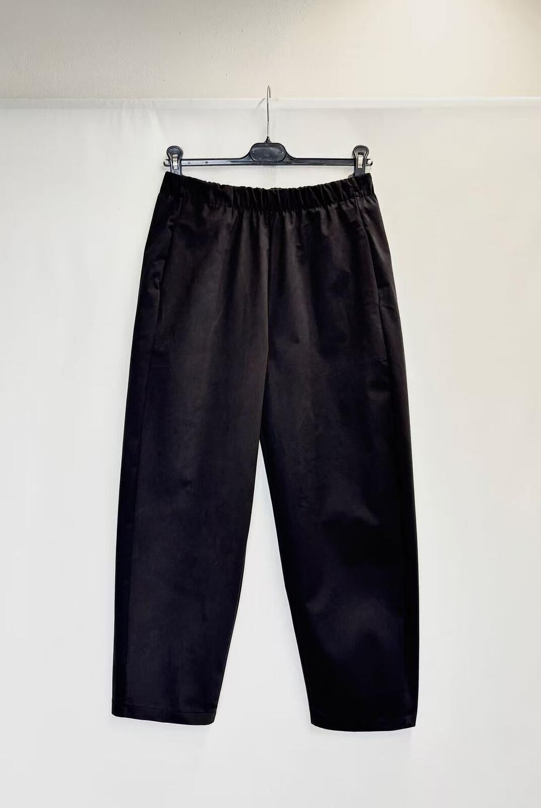 Black wide-leg cropped pants with an elastic waistband, hanging on a black hanger against a plain white wall.