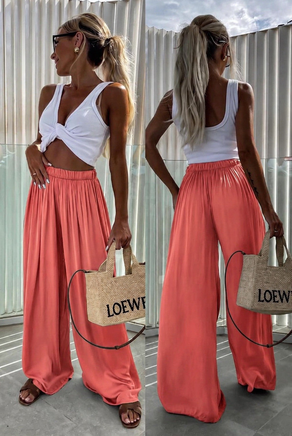 A woman shown from the front and back wearing a white twisted-strap crop top and flowing coral wide-leg pants, standing outdoors against a corrugated metal wall and holding a woven Loewe tote bag.
