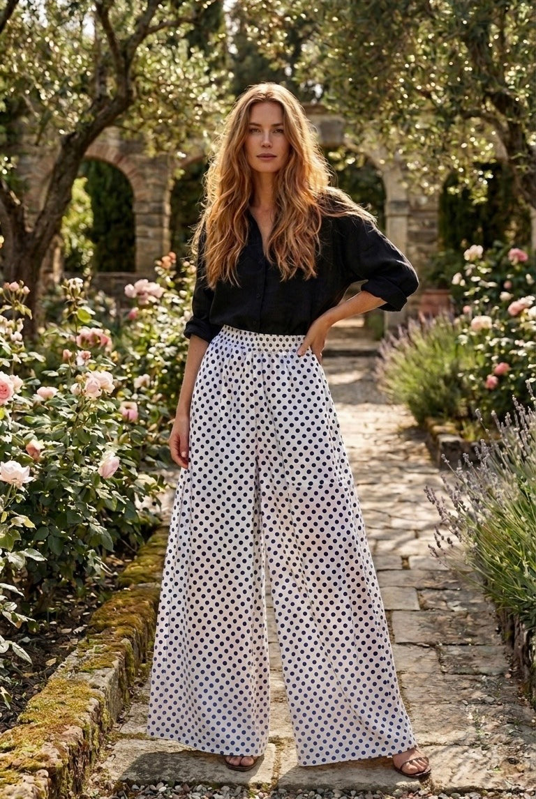 Woman in a black top and white polka dot pants standing in a garden.