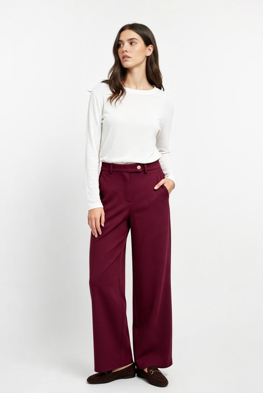 A woman modeling a white long-sleeve top and deep burgundy wide-leg trousers, paired with dark brown loafers, against a plain white studio background.